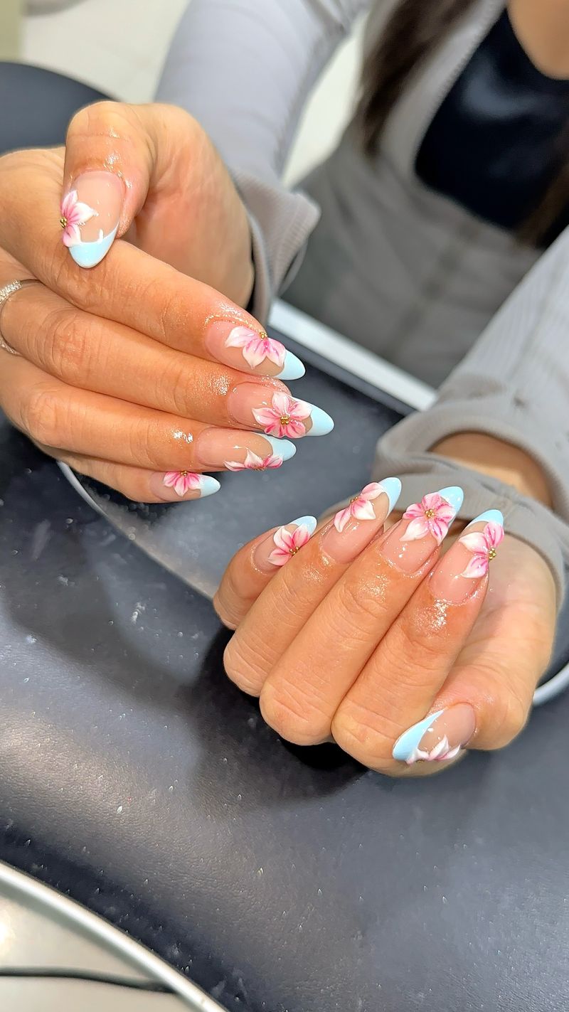 Almond nails with pastel blue French tips and hand-painted pink flowers at Shella Nails & Lashes, Da Nang